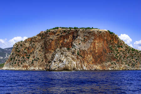 Rock with an ancient stone wall of Alanya Castle (Turkey) on top - view from the Mediterranean Sea. Seascape with an ancient fortress over a steep desert cliff against a background of blue waterのeditorial素材