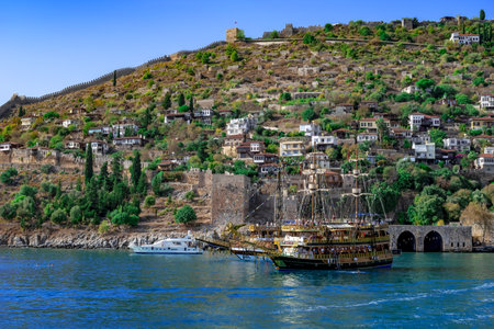 Alanya, Turkey - October 22, 2020: Pirate ship for parties in Mediterranean Sea against the background of Alanya old town. Seascape with ruins of ancient buildings, medieval wall and modern cottagesのeditorial素材