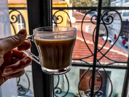 Female hand holding a cup of coffee on the background of a blurred landscape of Istanbul (Turkey) street outside the window. Morning coffee in the tourist townの写真素材