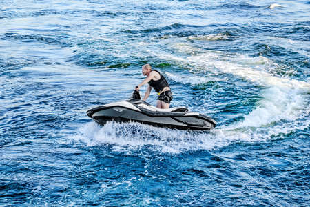 Kherson, Ukraine - July 22, 2020: A young man cuts the waves on a jet ski in the Dnieper River in Kherson. A male sportsman glides on blue water to advertise water activitiesのeditorial素材
