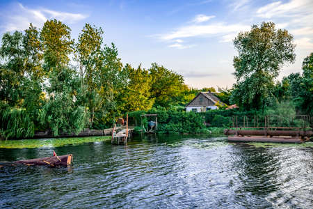 View from the water to a settlement on the coast of the Konka River in Kherson (Ukraine). Country house among summer greenery and a private pier in a swampy reservoirの写真素材