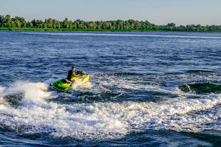 Kherson, Ukraine - July 22, 2020: A man has fun on a personal watercraft in the Dnieper River off the coast of Kherson. An adult on a Jet Ski leaves a trail of white foam on blue waterのeditorial素材