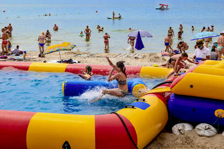 Zaliznyi Port, Ukraine - July 23, 2020: Children have fun on an inflatable rubber water slide on the beach in Zaliznyi Port. Beach activities in the resort Ukrainian villageのeditorial素材