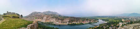 Panorama of the Buna river valley - view from the wall of the Shkoder castle (Albania). Beautiful widescreen landscape with the ruins of an ancient fortress, mountains, plain, river and city on the horizonの写真素材