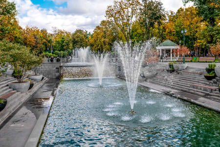 Cascade lake with fountains in the Shevchenko City Garden in Kharkiv (Ukraine). Beautiful autumn landscape with a pond, a waterfall and a fountain among the parkの写真素材