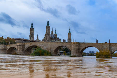 Puente de Piedra bridge over Ebro river with yellow water against the backdrop of the towers of Cathedral-Basilica of Our Lady of the Pillar in Zaragoza, Spain. Autumn cityscape of spanish cityの写真素材