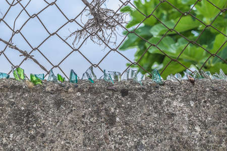 Pieces of glass on top of a cement fence with mesh in Albania. Homemade protective system for home securityの写真素材