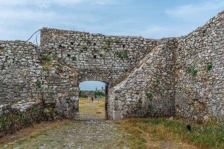 Shkoder, Albania - June 21, 2021: Ancient stone wall with a gate and a group of tourists walk among...
