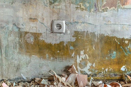 European electrical socket on the wall without wallpaper and pieces of paper lie on the floor. Replacement of wallpaper in the apartment. Background with copy spaceの写真素材