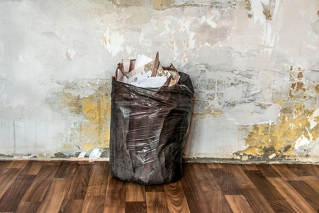 A black trash bag filled with old torn wallpaper stands against a plastered wall in an apartment. Repair and garbage collection in the room. Architectural backgroundの写真素材