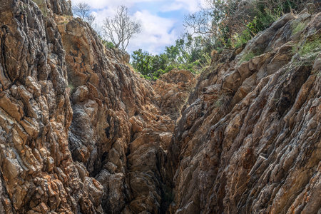 Bottom view of the gorge with layered walls on Mogren beach in Budva, Montenegro. View from the canyon to stone mineral formations on the background of a cloudy sky and summer greenery above the cliffの写真素材