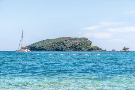 The yacht sails off the coast of the Sveti Nikola island - view from Budva, Montenegro. Seascape with the island of St. Nicholas among the blue water of the Adriatic Sea in the summer in the Balkansの写真素材