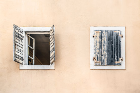 Closed and open window on a beige wall, close-up. Two antique windows with wooden shutters on a building in the Old Town of Budva, Montenegro. Element of old architecture in Stari Gradの写真素材
