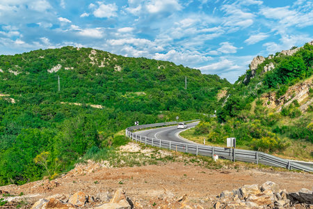 A car drives along the winding road of the M2.3 highway in Podostrog near Budva, Montenegro. Traffic on a mountain road among the forest in summer in the Balkansの写真素材