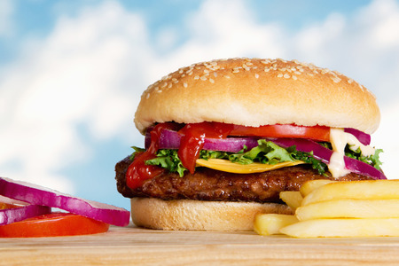 Stock image of cheeseburger with fries outdoors on wooden plate の写真素材