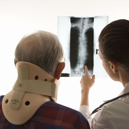 Over the shoulders view of mid-adult Caucasian female pointing at an x-ray as elderly Caucasian male...
