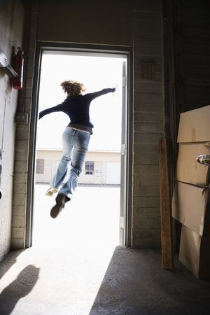 Woman running and jumping through open door from building to sunny outside.