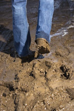 Close up of person walking in mud wearing jeans and boots.