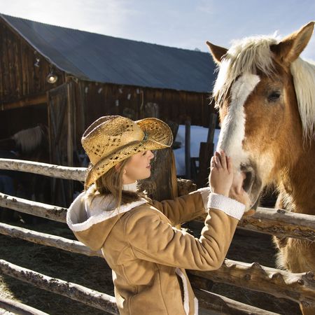 Young Caucasian woman petting horse with stable in background.の写真素材