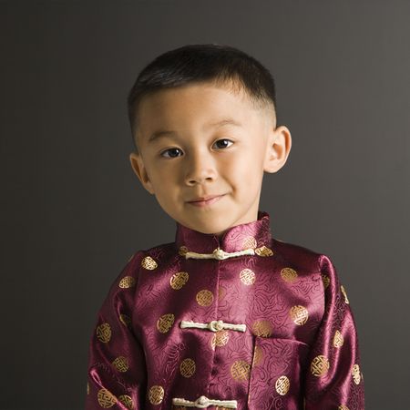 Asian boy in traditional attire standing against black background.の写真素材
