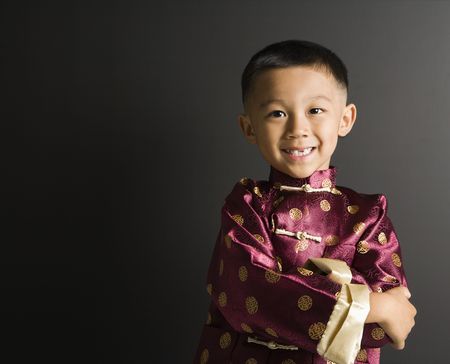 Asian boy in traditional attire standing against black background.の写真素材