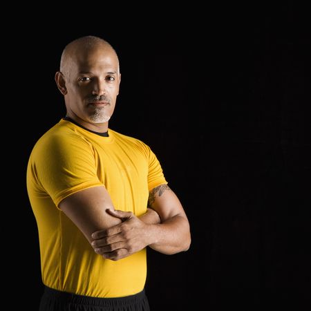 Mid adult multiethnic man wearing yellow exercise shirt with arms crossed looking at viewer.の写真素材
