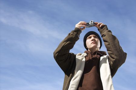 Caucasian male teenager taking a picture with a digital camera.