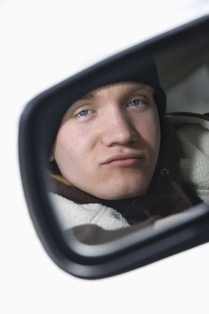 Caucasian male teenager looking at himself in side view mirror of car.