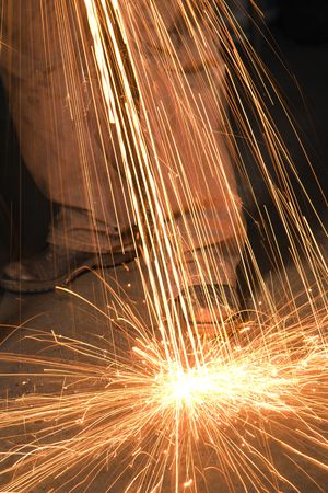 Caucasian male metalsmith shaping metal and creating sparks.