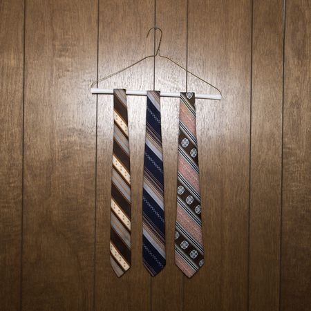 Three retro ties hanging on a wire hanger against wood paneling.の写真素材
