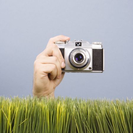 Studio shot of Caucasian male hand holding vintage camera with grass in foreground.
