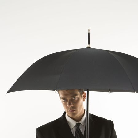 Caucasian mid-adult businessman  looking out at viewer from under umbrella.の写真素材