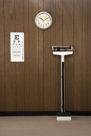 Retro doctor's office with wood paneling, clock, eye chart and scale.の写真素材