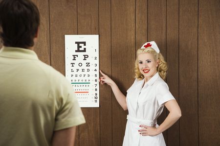Caucasian mid-adult female nurse  pointing out eye chart to mid-adult male patient.