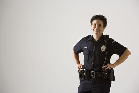 Portrait of mid adult Caucasian policewoman standing with hands on gun holster looking at viewer smiling.の写真素材