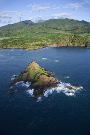 Aerial of rock jutting out of Pacific ocean off the coast of Maui, Hawaii with mountain landscape in background.の写真素材