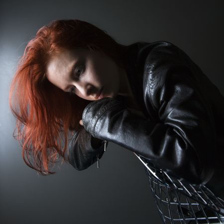 Pretty redhead young woman wearing leather jacket hanging over back of chair.の写真素材