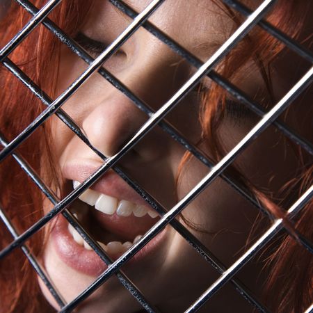 Pretty redhead young woman face with mouth open behind metal pattern.の写真素材