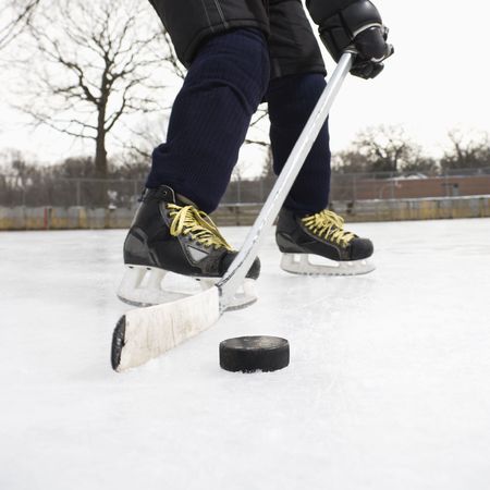 Boy in ice hockey uniform skating on ice rink moving puck.