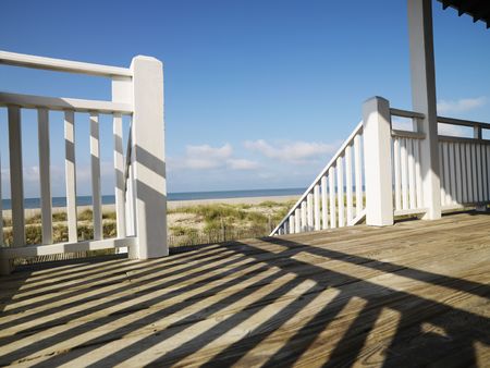 View of beach from porch with railing casting shadow on wooden deck at Bald Head Island, North...