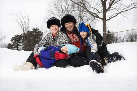 Portrait of happy Caucasian family of four sitting in snow smiling at veiwer.の写真素材