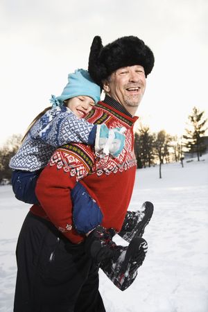 Caucasian middle aged man holding Caucasian litte girl piggyback style smiling and looking at viewer smiling.の写真素材