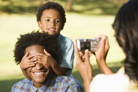 Woman photographing husband and son in park with digital camera.の写真素材