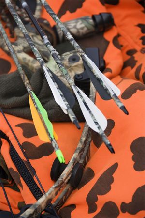 Still life shot of bow and arrows laying against blaze orange camouflage.