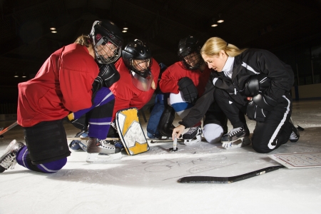Women hockey players on ice looking at game plan with coach.の写真素材