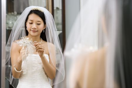 Asian bride looking at bouquet in mirror.の写真素材