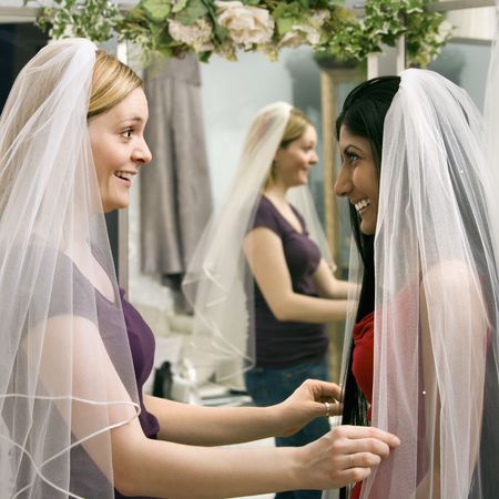 Indian woman and Caucasian woman trying on veils and looking in mirror.の写真素材