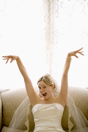 Caucasian bride on love seat with arms raised and joyful expression.の写真素材