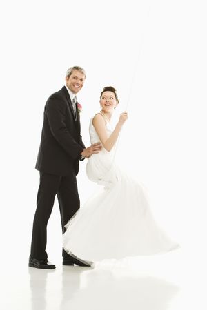 Portrait of Caucasian groom pushing Asian bride in swing.の写真素材