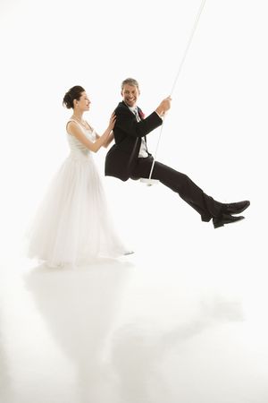 Asian bride pushing Caucasian groom in swing set.の写真素材